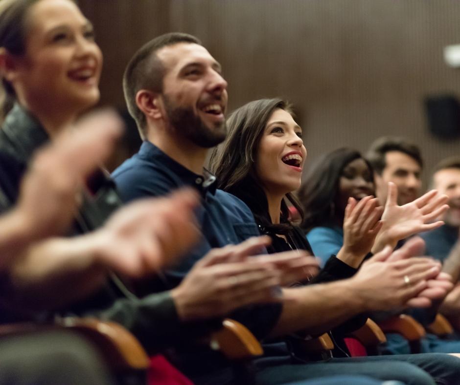 Audience members laughing and applauding at a live performance