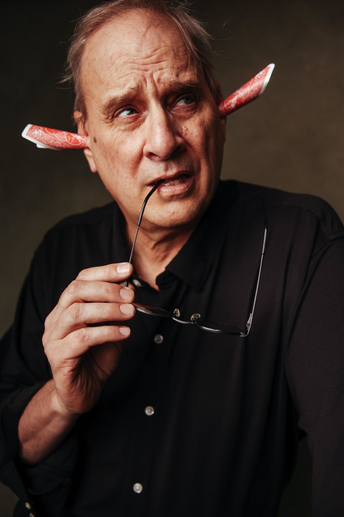David Williamson with playing cards tucked behind his ears, chewing on his glasses and looking skeptical